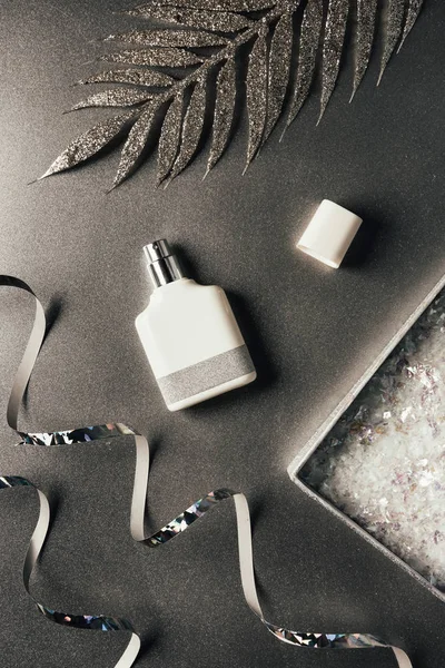 Top view of perfume bottle, silver ribbons and shiny decorative leaves on grey — Stock Photo