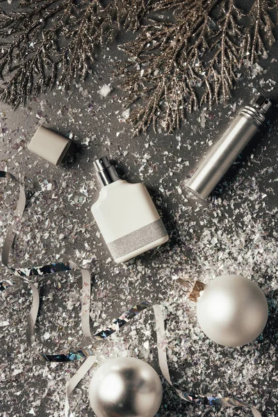 Vista superior de perfumes embotellados y adornos de Navidad brillantes en gris - foto de stock