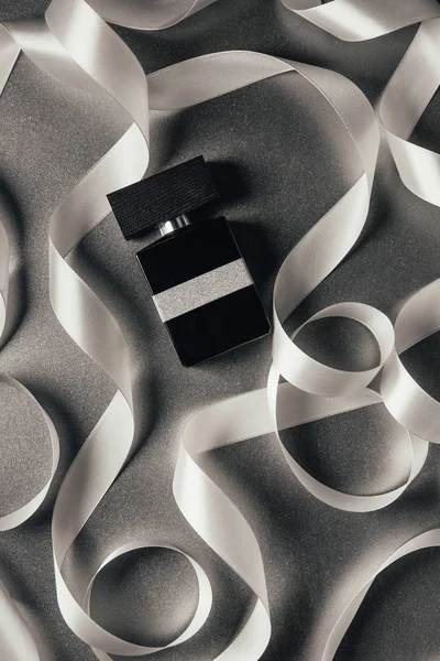 Vista superior de perfume embotellado y cintas blancas en gris - foto de stock