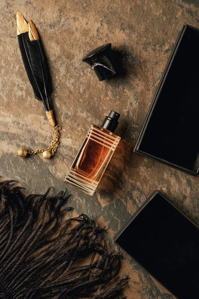 Vista superior de perfume y plumas negras decorativas sobre superficie envejecida marrón - foto de stock