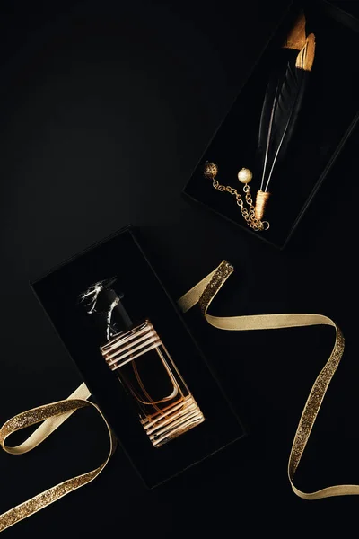 Top view of perfume bottle with golden ribbon, gift box and decorative feathers on black — Stock Photo