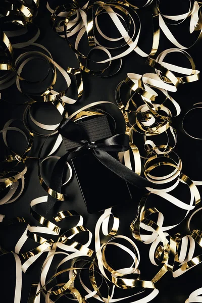 Top view of black perfume bottle with golden ribbons on black — Stock Photo