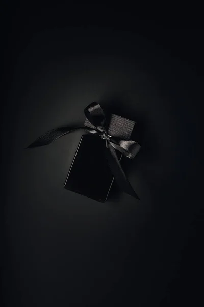 Top view of black perfume bottle with ribbon on black background — Stock Photo