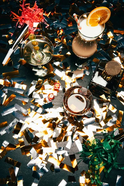 Vista desde arriba de cócteles alcohólicos, whisky y cuernos de fiesta en la mesa cubierta por confeti dorado - foto de stock