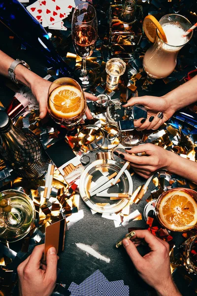 Image recadrée de l'homme avec carte de crédit et billet roulé va renifler la cocaïne tandis que ses amies célébrant avec de l'alcool et des cigarettes à la table couverte de confettis dorés — Photo de stock