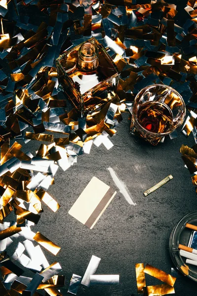 Vue du dessus du whisky, du billet roulé, de la carte de crédit et de la cocaïne sur la table couverte de confettis dorés — Photo de stock