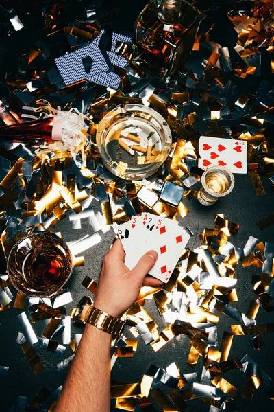Imagem cortada do homem com cartas de jogo e álcool sentado à mesa coberto por confetes dourados — Fotografia de Stock