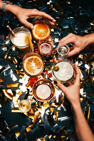 Partial view of friends clinking by cocktail glasses at table covered by golden confetti — Stock Photo