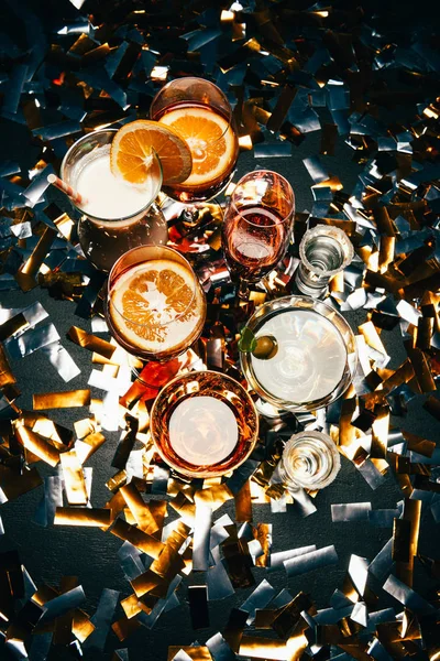 Flach mit verschiedenen alkoholischen Cocktails und Partyhörnern auf einem mit goldenem Konfetti gedeckten Tisch — Stockfoto