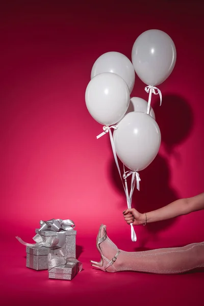 Cropped image of girl sitting and holding bundle of white balloons with helium on burgundy — Stock Photo