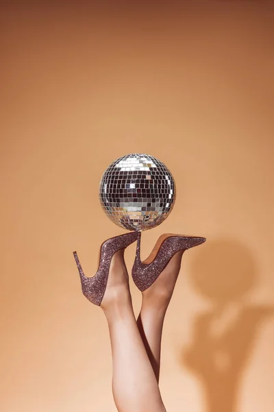 Cropped image of woman holding shiny disco ball on high heels at party on beige — Stock Photo