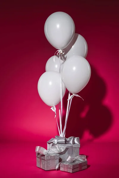 Bundle of white balloons and silver gift boxes on burgundy — Stock Photo