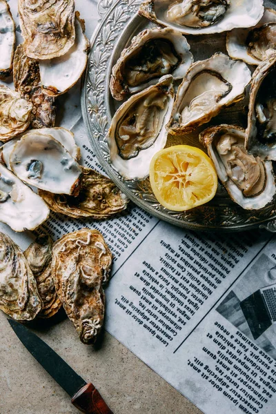 Flat lay com ostras, limão e faca no jornal na superfície cinza — Fotografia de Stock