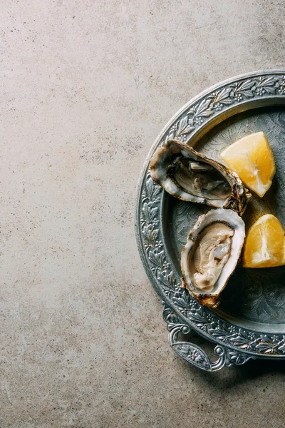 Vista superior de ostras e pedaços de limão na bandeja de metal na mesa cinza — Fotografia de Stock