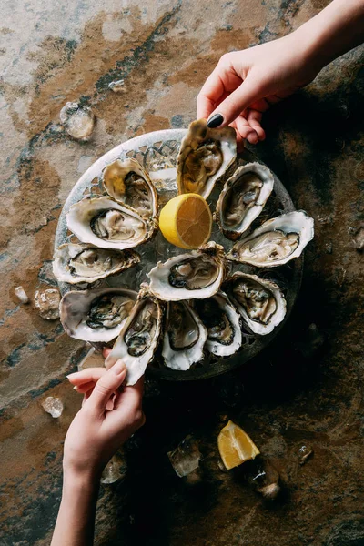 Partial view of women at grungy tabletop with oysters, ice and lemon — Stock Photo