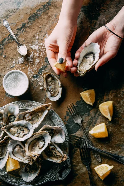 Cropped shot of woman holding oyster and lemon piece in hand at grungy tabletop — Stock Photo