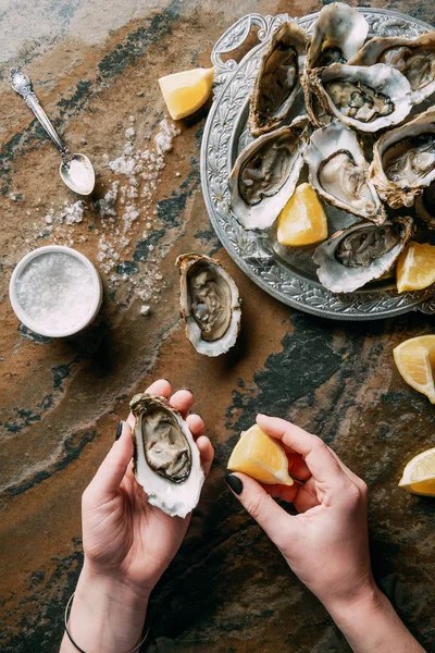 Plan recadré d'une femme tenant une huître et un morceau de citron à la main à la table grungy — Photo de stock