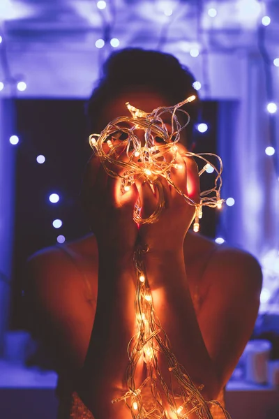 Visión oscura de la mujer sosteniendo luces festivas en las manos en casa — Stock Photo