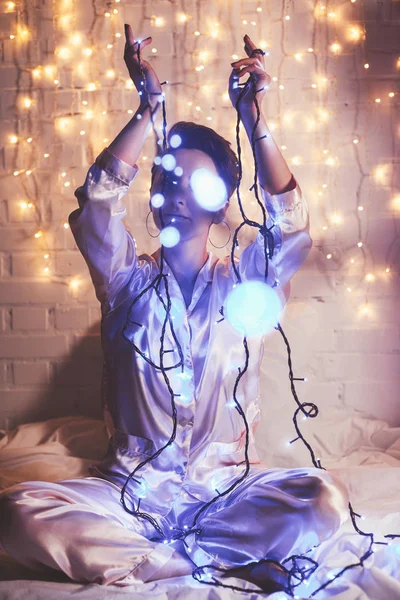 Mulher de pijama descansando na cama com luzes de Natal ao redor — Fotografia de Stock
