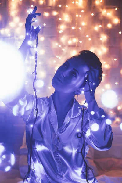 Woman in pajamas resting on bed with christmas lights around — Stock Photo