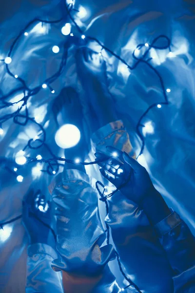 Vista parziale della donna in pigiama sul letto con luci festive blu intorno — Foto stock