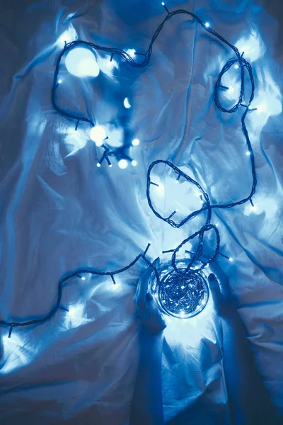 Vue partielle de la femme tenant un pot en verre avec des lumières de Noël bleues autour sur le lit — Photo de stock