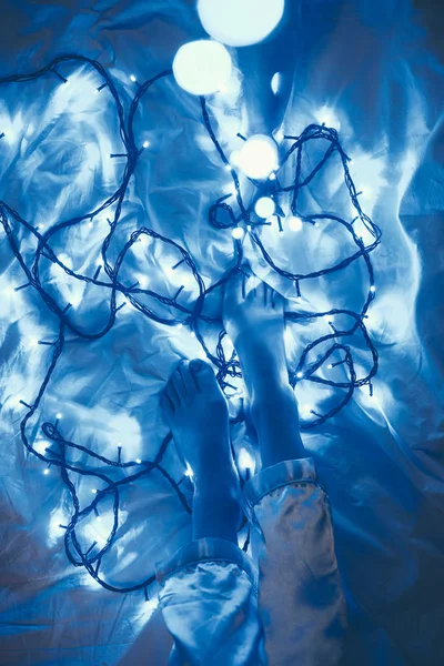 Cropped shot of woman in pajamas on bed with blue christmas lights around — Stock Photo