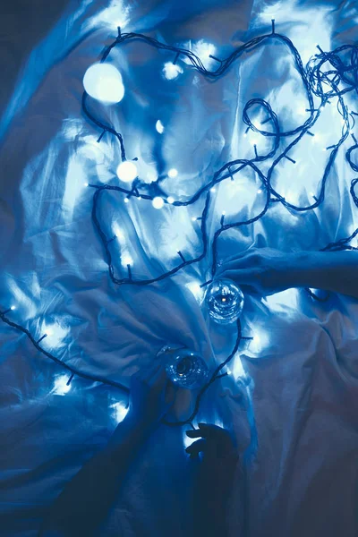 Partial view of women with glasses of champagne on bed with blue festive lights — Stock Photo