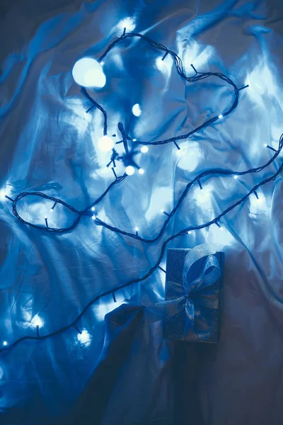 Cropped shot of woman and wrapped christmas gift on bed with blue festive lights — Stock Photo