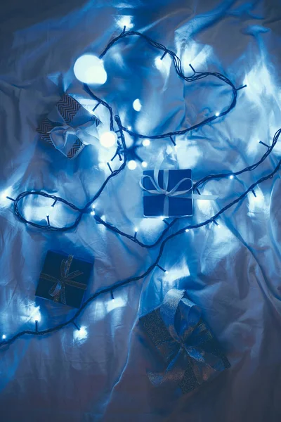 Flat lay with wrapped christmas gifts and festive lights on bed — Stock Photo