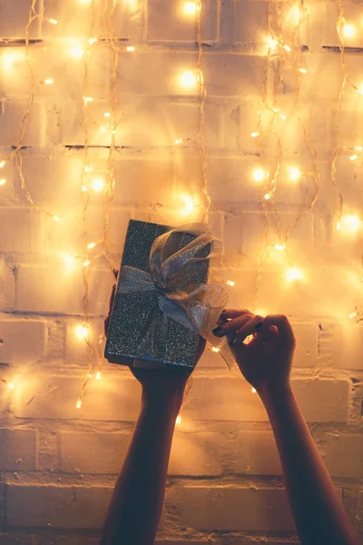 Vista parcial de la mujer sosteniendo regalo envuelto con luces de Navidad detrás - foto de stock