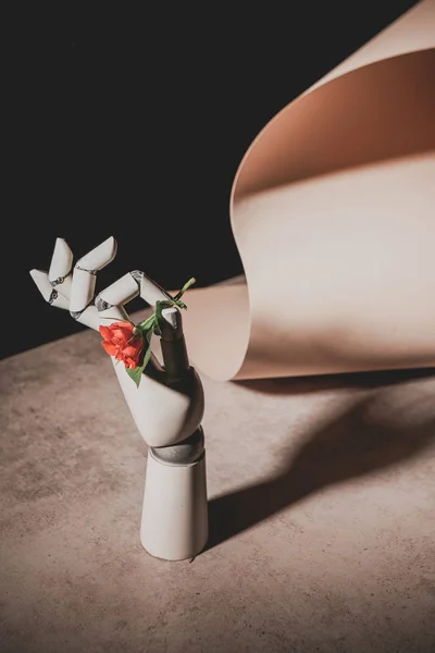 Pink rose flower in robotic hand on stone table with sheet of paper isolated on black — Stock Photo