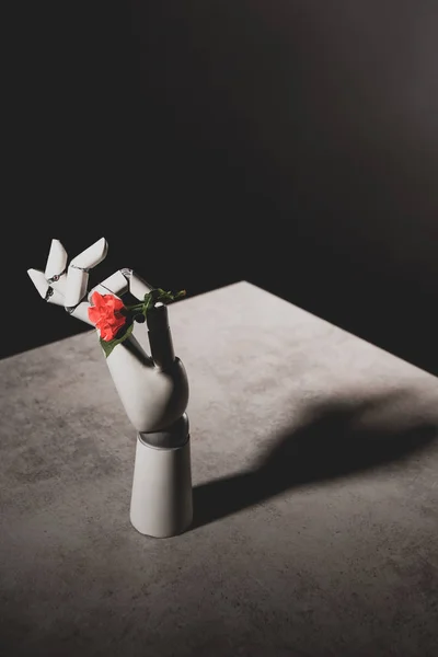 Pink rose flower in robotic hand on stone table on black background — Stock Photo