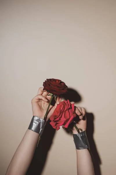 Partial view of woman with taped red rose flowers on beige background — Stock Photo