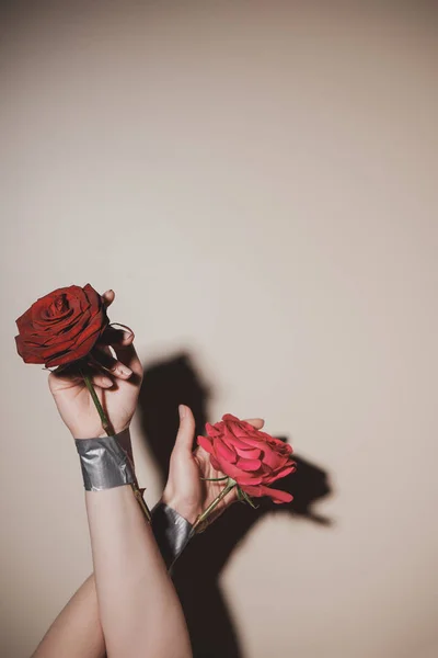 Partial view of woman with taped red rose flowers on beige background — Stock Photo