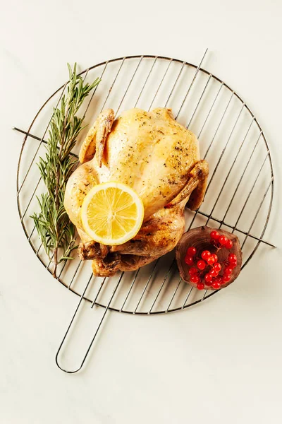Vista superior de frango frito, alecrim e bagas na grade de metal com limão na mesa branca — Fotografia de Stock