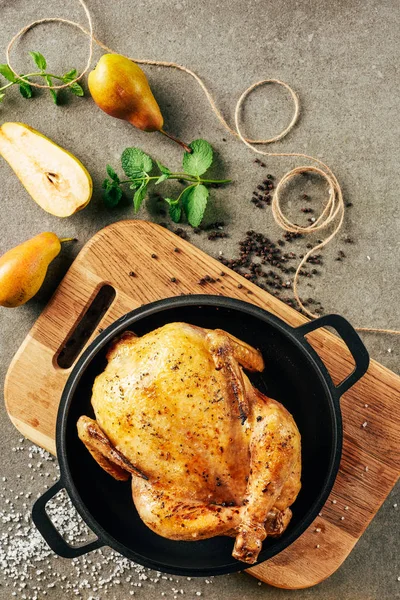 Вид сверху на жареную курицу в сковороде с грушами, веревками и зеленью — стоковое фото