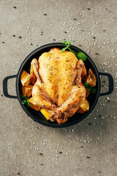 Vue du dessus du poulet frit dans une plaque chauffante avec des citrons et de la verdure sur la surface en pierre — Photo de stock