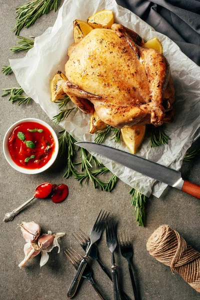 Vue du dessus du poulet frit avec des citrons sur tissu avec couteau, sauce, fourchettes et romarin — Photo de stock