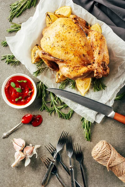 Pollo frito con limones sobre tela con cuchillo, salsa, tenedores y romero - foto de stock