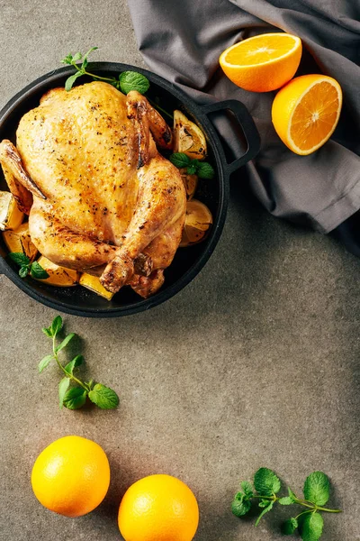 Верхний вид жареной курицы в сковороде с апельсинами, зеленью и тканью — стоковое фото