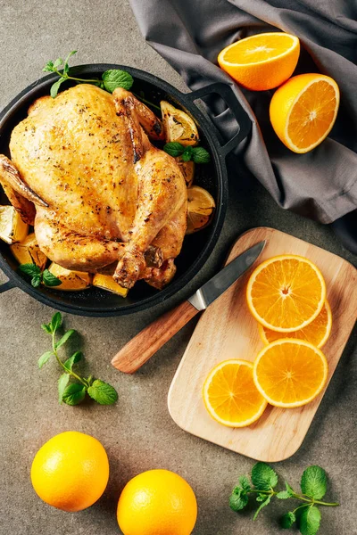 Oranges cliced sur planche à découper avec couteau et poulet frit dans la poêle — Photo de stock