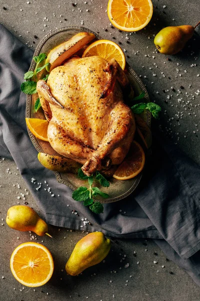 Верхний вид жареного цыпленка с апельсинами, грушами и зеленью на лоток и ткань — стоковое фото