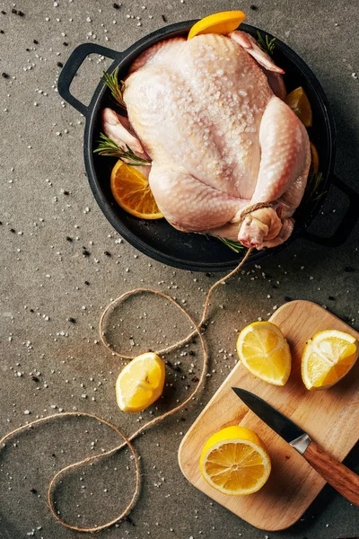 Pollo crudo con naranjas y especias en sartén y tabla de cortar con limones y cuchillo - foto de stock