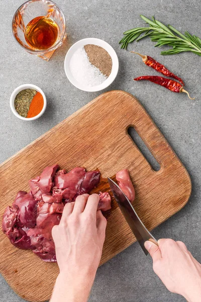 Vista recortada de la mujer cortando carne cruda en la tabla de cortar entre especias, vidrio de coñac, pimientos y romero - foto de stock
