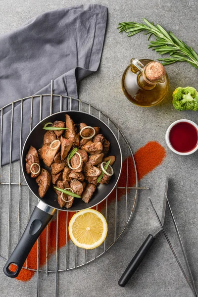 Vista dall'alto di carne fritta in padella e limone su griglia metallica con olio, broccoli e salsa — Foto stock