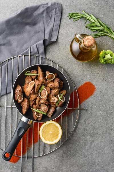 Fried meat in fried pan and lemon on metal grille with oil, broccoli and sauce — Stock Photo