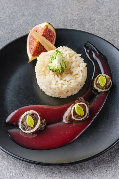 Rice, broccoli, fig and fried meat with sauce on black plate and stone surface — Stock Photo