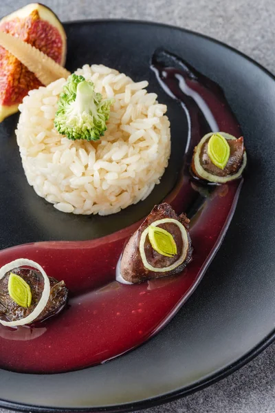 Close up of rice, broccoli, fig and fried meat with sauce on black plate — Stock Photo