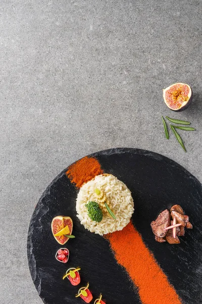 Вид зверху на рис, брокколі, інжир та смажене м'ясо з соусом на чорній тарілці — стокове фото